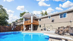 A residential backyard with a swimming pool, a wooden deck, and a covered patio area. - Pool, Sauna, Work out area, ping pong, King Bed.  So Many Amenities!!! (Omaha)