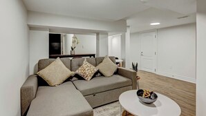 Un salon moderne avec un canapé d’angle gris, une petite table blanche et un plancher en bois.
