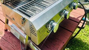 Ein tragbarer Gasgrill mit Bedienfeld auf einer Holzterrasse.