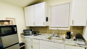 Eine kleine Küche mit weißen Schränken, einer Mikrowelle, einem Toaster und einem Spülbecken.