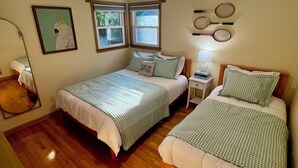 Una habitación con dos camas individuales, una lámpara de techo, un cuadro enmarcado y una ventana con persianas.