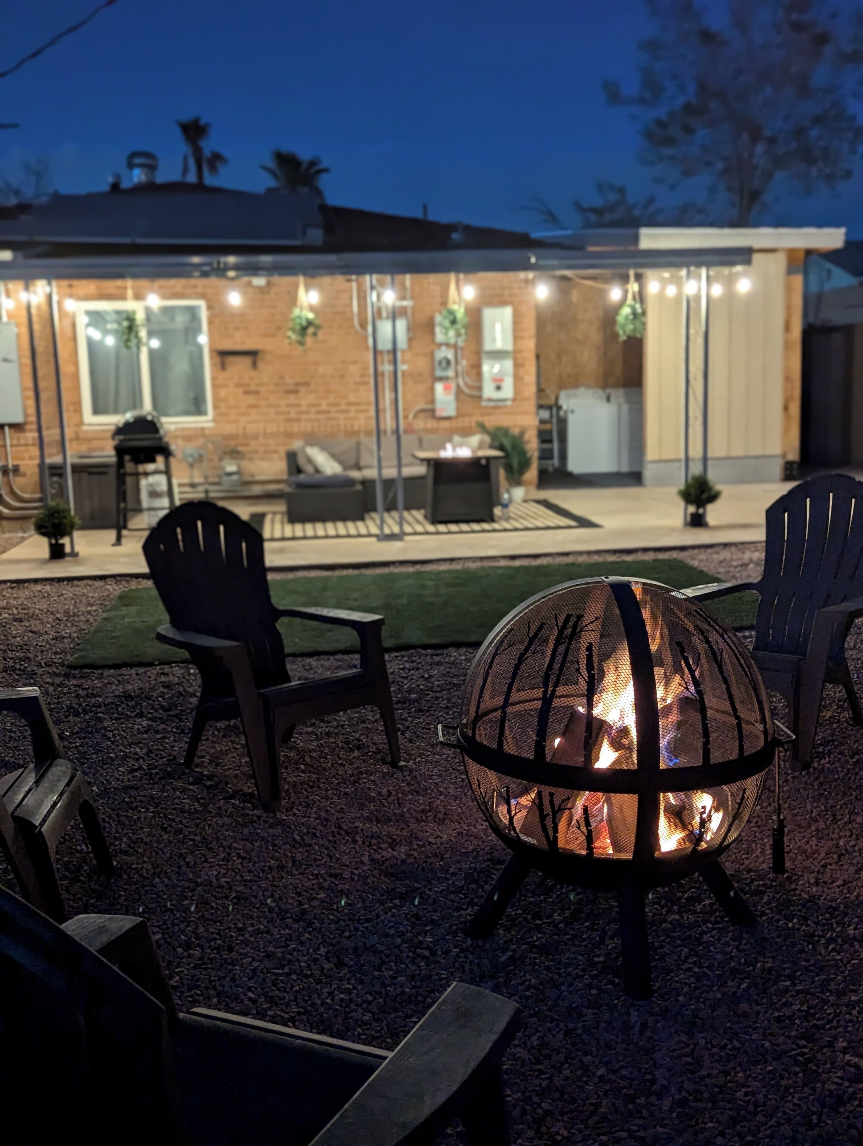 Ein Patio mit Feuerstelle, Sitzgelegenheiten im Freien und einem Backsteinhaus im Hintergrund.