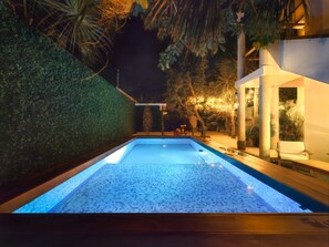 A swimming pool with a tiled floor, surrounded by a low wall and palm trees. - SAYU - Suites (Cozumel)