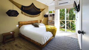 A bedroom with a bed, a hanging light, a ceiling fan, a TV, and a view of greenery outside. - SAYU - Suites (Cozumel)