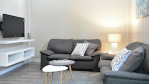 Una sala moderna con un sofá gris, una mesita redonda y un televisor montado.