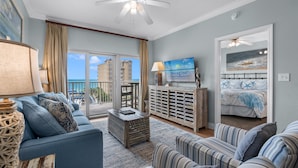 A living room with a sofa, armchairs, a coffee table, a TV, and a painting. - Lazy River, 3 Pools - Crystal Tower - Free Daily Activities & Beach Service! (Gulf Shores)