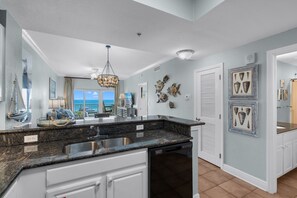 A kitchen with a built-in dishwasher, a large island with a sink, and decorative wall art. - Lazy River, 3 Pools - Crystal Tower - Free Daily Activities & Beach Service! (Gulf Shores)