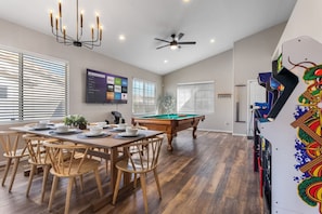 A dining area with a pool table, wooden chairs, a ceiling fan, and a TV displaying streaming services.