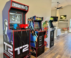 Arcade machines in a room with a ceiling fan, a TV, and a fireplace.