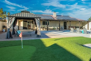 A covered outdoor seating area with a pergola, a pool table, and lounge chairs.