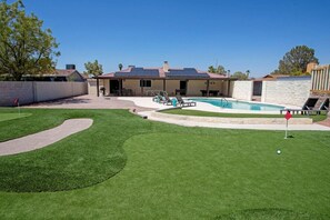A residential property with a swimming pool, a patio area with outdoor furniture, and a well-maintained lawn.