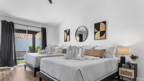 A hotel room with two beds, a large window with curtains, a round mirror, and abstract wall art.