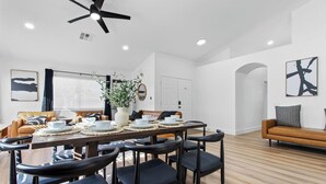A modern dining area with a wooden table, black chairs, and a ceiling fan.