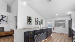 A modern kitchen with a central island, black cabinets with gold handles, and artwork on the walls.