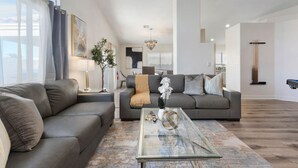 A modern living room with a sofa, coffee table, and a view of the outdoors. - 4BR Getaway w/Pool and Billiard! (North Las Vegas)