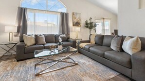 A living room with two sofas, a glass coffee table, and a large window with curtains. - 4BR Getaway w/Pool and Billiard! (North Las Vegas)