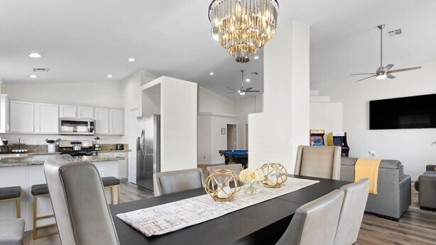 A modern kitchen with white cabinets, a stainless steel refrigerator, and a dining area with a dark table and chairs. - 4BR Getaway w/Pool and Billiard! (North Las Vegas)
