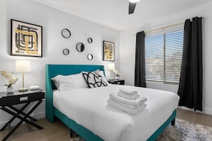 Et moderne hotelværelse med en teal seng, hvide sengetæpper og billedkunst på væggene.