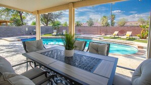 Une terrasse couverte avec une piscine, des sièges d’extérieur et une vue sur le jardin arrière.