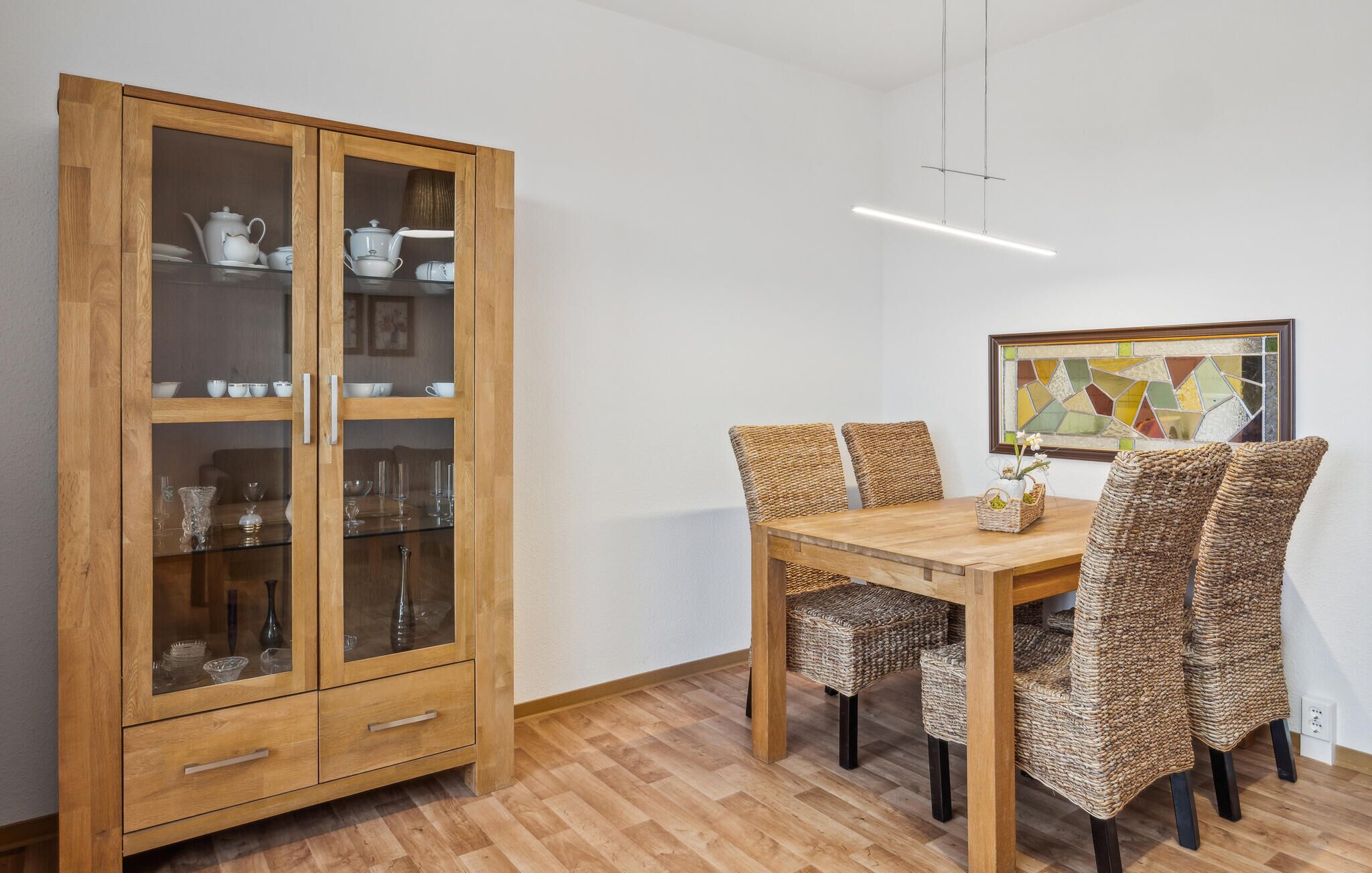 A dining area with a wooden cabinet, wicker chairs, and a table.