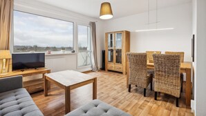 A modern living room with a TV, sofa, dining table, wicker chairs, and a cabinet. - 1 bedroom cozy apartment in Anklam (Anklam)