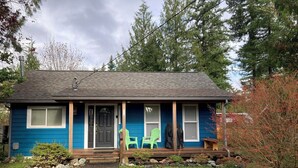 A small, single-story house with a dark blue exterior, a front porch with steps, and a green chair outside. - Music Place Guest House (Maple Falls)