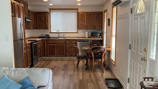 A compact kitchen with wooden cabinets, a refrigerator, microwave, and a dining area with a table and chairs. - Music Place Guest House (Maple Falls)