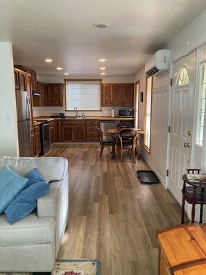 A compact kitchen with wooden cabinets, a refrigerator, microwave, and a dining area with a table and chairs. - Music Place Guest House (Maple Falls)