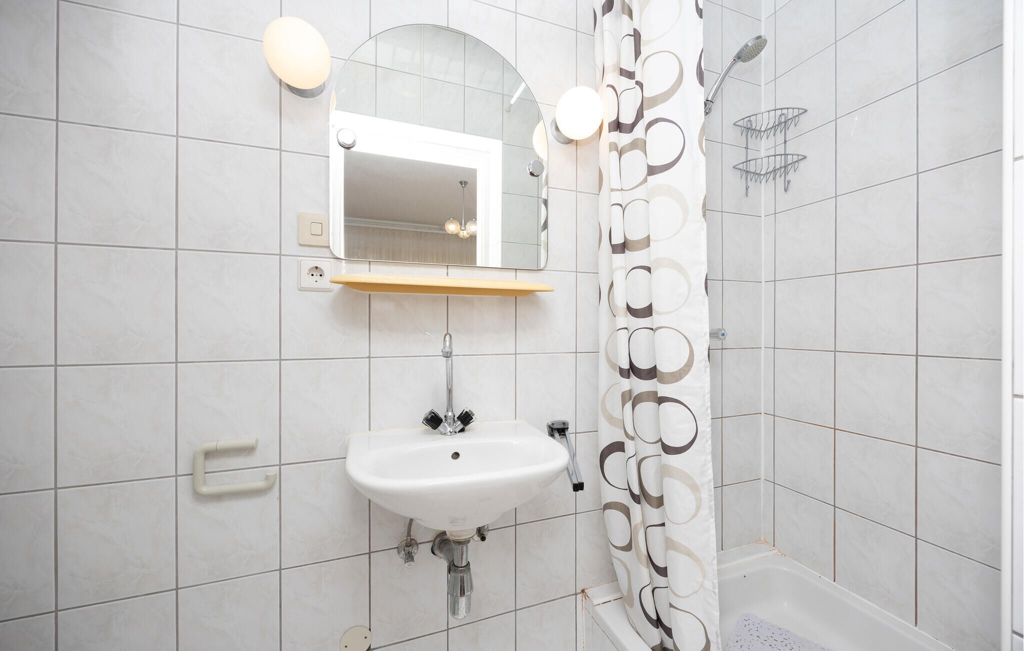 Ein Badezimmer mit weißem Waschbecken, einem Spiegel, einer Dusche und einem Handtuchhalter.