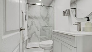 Een moderne badkamer met een glazen douchecabine, een wit toilet en een wastafel met spiegel en zeepdispenser.