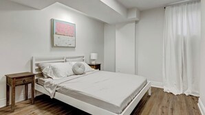Een moderne slaapkamer met een wit bed, houten vloer en een nachtkastje.