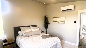 A bedroom with a bed, nightstand, wall-mounted air conditioner, and a door.