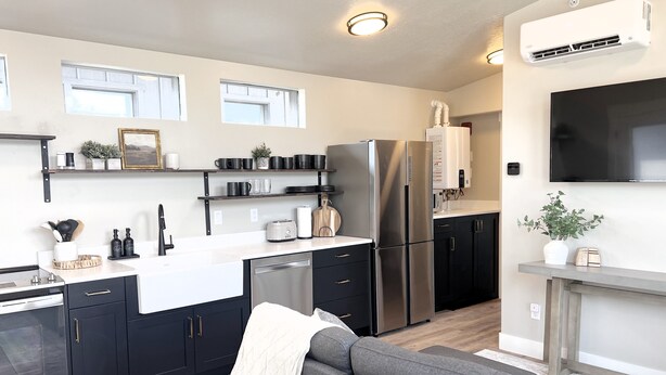 A modern kitchen with black cabinets, stainless steel appliances, and a grey sofa in the living area.