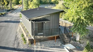 A small, modern building with a sloped roof, a balcony, and a staircase leading to an upper level.