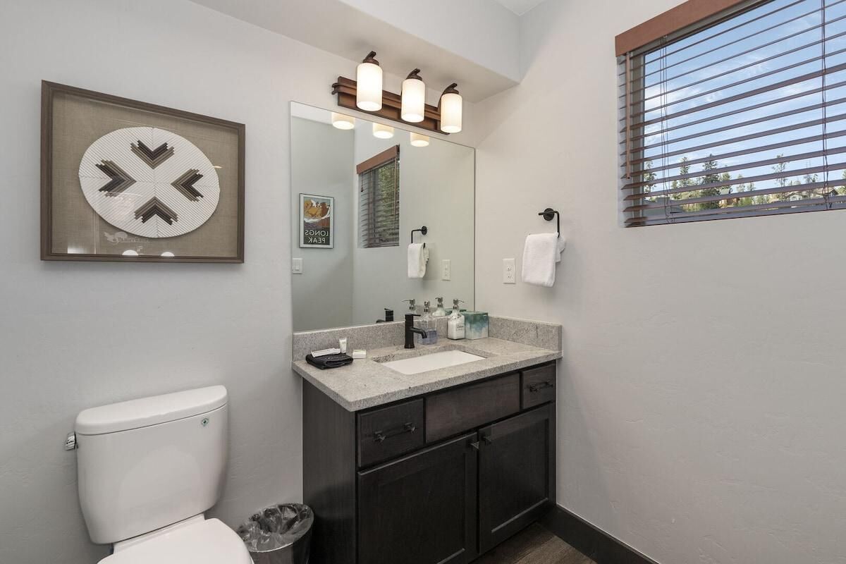 A bathroom with a toilet, sink, mirror, and window.