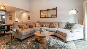 A living room with a sectional sofa, a round coffee table, a patterned rug, a mirror, and a floor lamp.