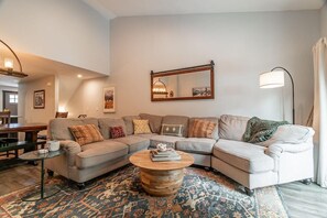 A living room with a sectional sofa, a round coffee table, a patterned rug, a mirror, and a floor lamp.