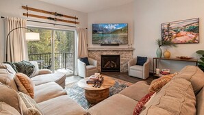 A living room with a fireplace, a television, and a balcony with curtains.