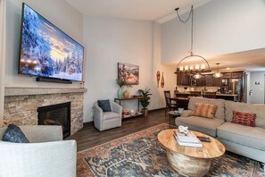 A living room with a fireplace, a television, a sofa, a coffee table, and a dining area.