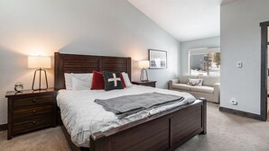 A bedroom with a large bed, bedside tables, a nightstand, a lamp, a couch, and a window.