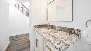 Ein Badezimmer mit Marmorwaschbecken, einem großen Spiegel und einer Holztreppe im Hintergrund.