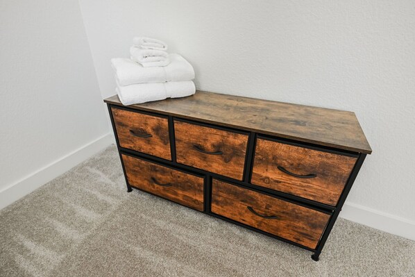 A wooden dresser with four drawers and a top shelf, placed against a white wall.
