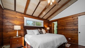 Un dormitorio con paneles de madera, una cama, mesitas de noche y un ventilador de techo.