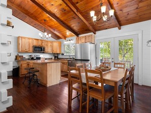 A modern kitchen with wooden cabinets, a central island, and a dining area with wooden chairs. - Hot Tub.  Trails, Trout, Turkeys and Morels. (Grayling)