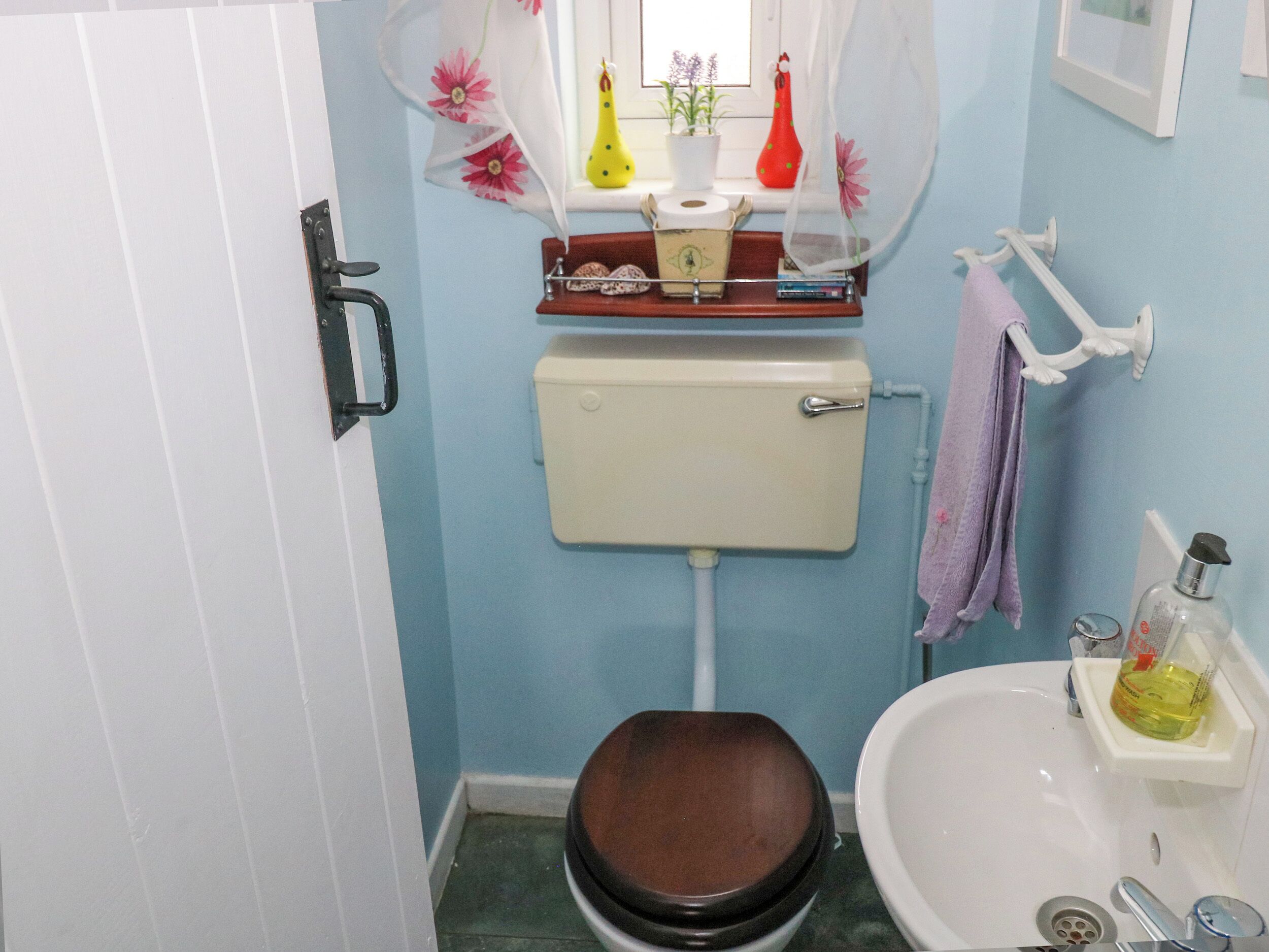 A small bathroom with a toilet, sink, and a window with decorative items.