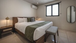 A bedroom with a wooden bed, a bedside table, a bench, a mirror, and a window. - Departamentos Central (Mérida)