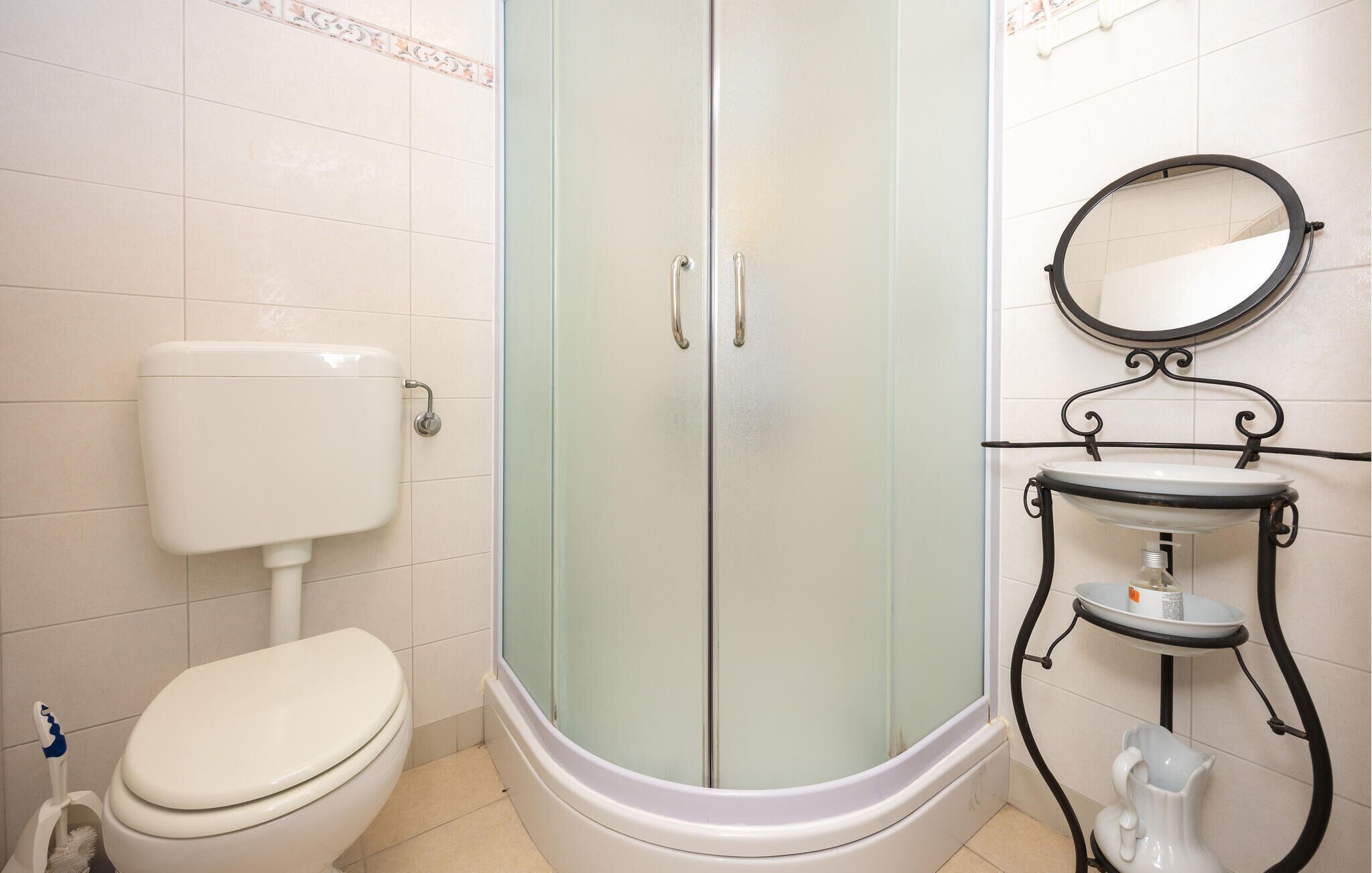 Een badkamer met een toilet, een douche met glazen wand, een wastafel met spiegel en een toilettenkwast.