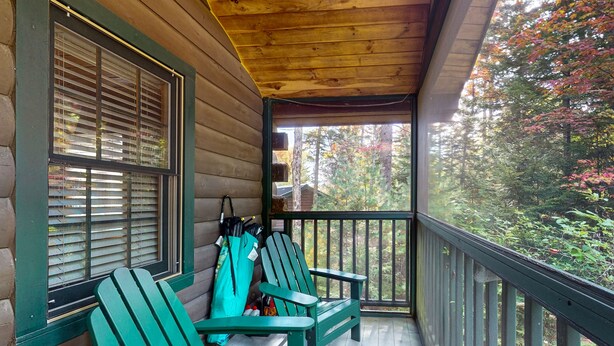 Un porche de cabaña de madera con dos sillas Adirondack verdes, una barandilla de madera y vista a un bosque.