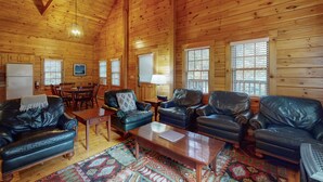 Interior acogedor de una cabaña de madera con sofás de cuero, un comedor y una alfombra estampada.