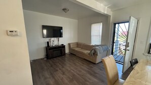 Una sala de estar con un televisor de pantalla plana, un sofá color beige, un mueble de entretenimiento de madera y un comedor con una mesa de mármol.